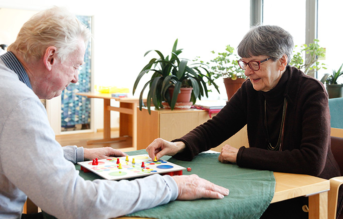 En äldre man och en äldre kvinna spelar Fia med knuff vid ett bord.