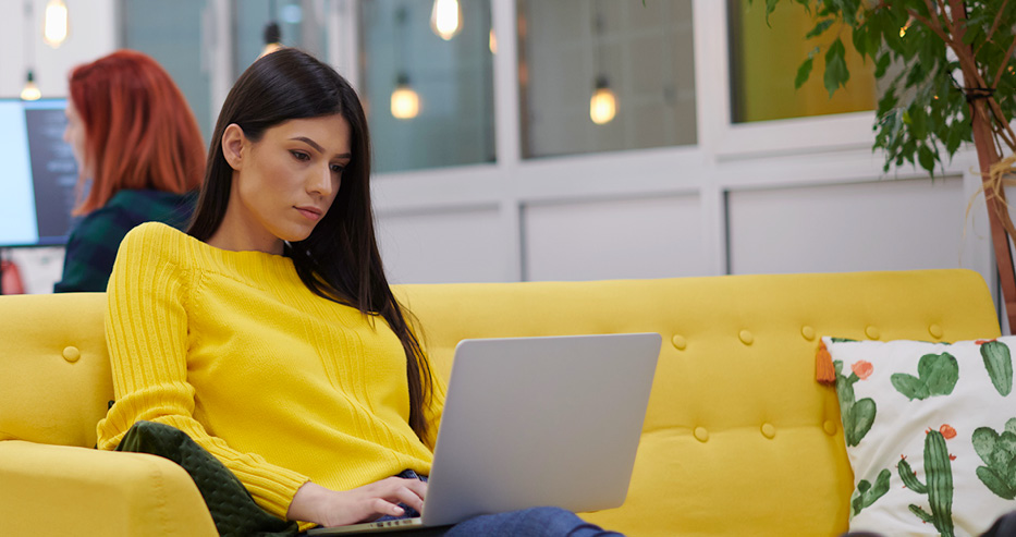 Kvinna i gul soffa med laptop i sitt knä