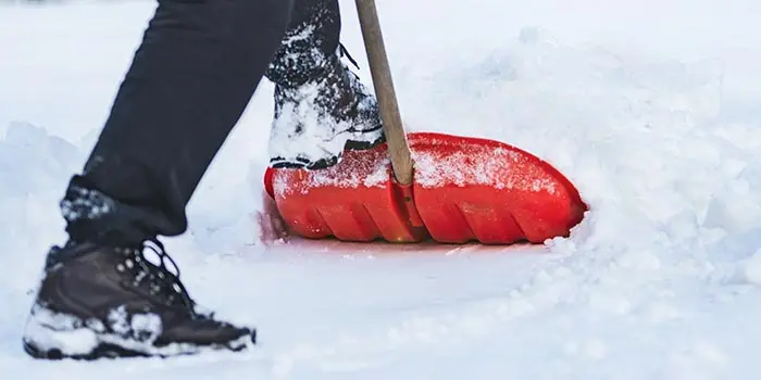 En person som skottar snö med en röd skyffel.