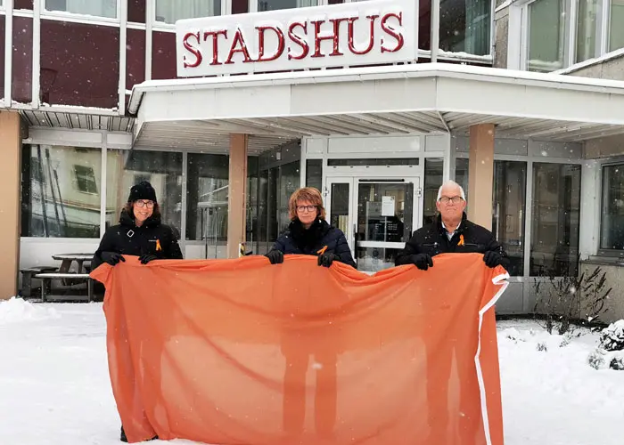 Tre personer som tillsammans håller i en orange flagga.