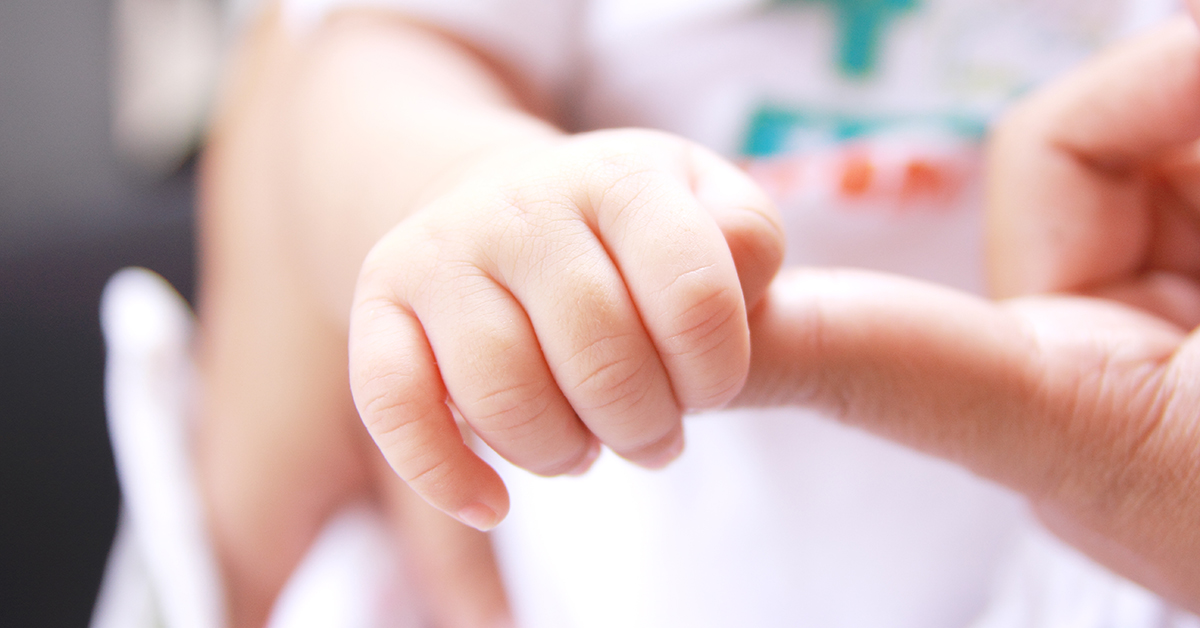 Ett litet barns hand som håller i en vuxens finger