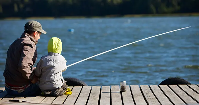 EN vuxen och ett barn som sitter på en brygga och fiskar.
