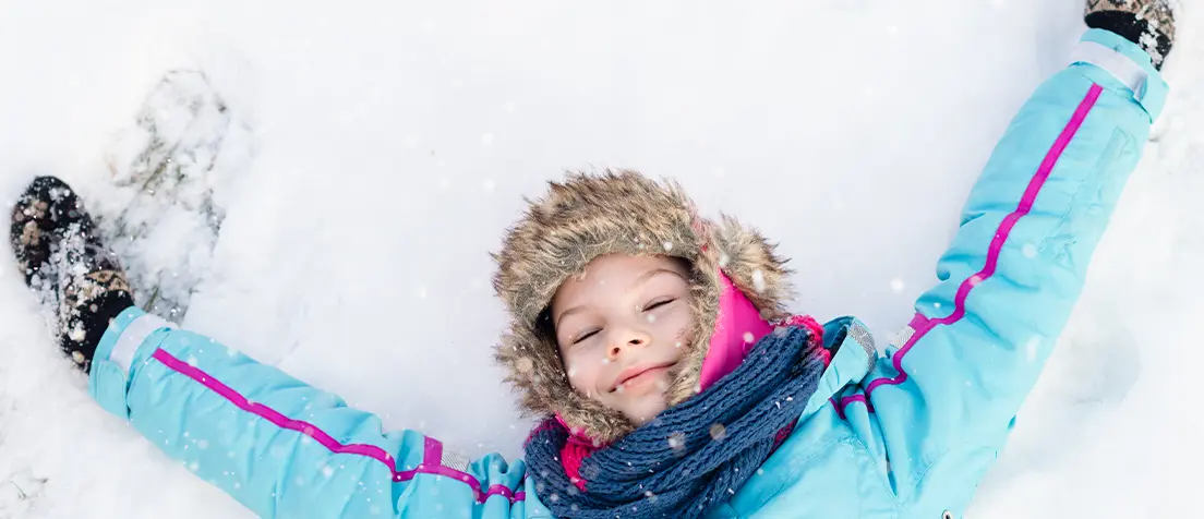 Glatt barn ligger i snön med armarna över huvudet