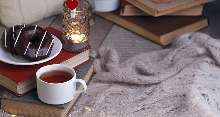 Högar med böcker, en kopp med te, ett värmeljus och en schal.