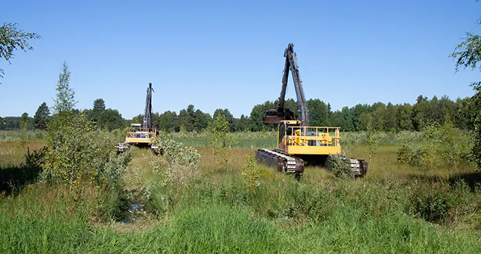 Två grävmaskiner på väg ut i våtmarksområdet